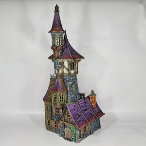 以下が含まれることがあります： 高い塔と複数のレベルを備えた、詳細なミニチュアファンタジー城。 城は紫色の屋根、石壁、小さな窓が特徴です。 全体的なデザインは気まぐれで詳細で、建築要素に焦点を当てています。