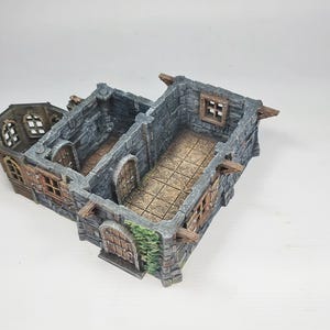 以下が含まれることがあります： グレーの石壁、茶色の木製アクセント、アーチ型のドアを備えた、ミニチュアの城の模型。 この模型は、詳細な窓と、テーブルゲームや展示に最適な質感のあるインテリアを備えています。