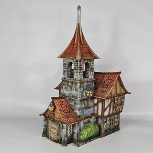 May include: A detailed miniature model of a medieval-style building. The structure features a tall central tower with a pointed roof, a stone facade, and a red tile roof. The building has multiple levels, windows, and decorative elements.