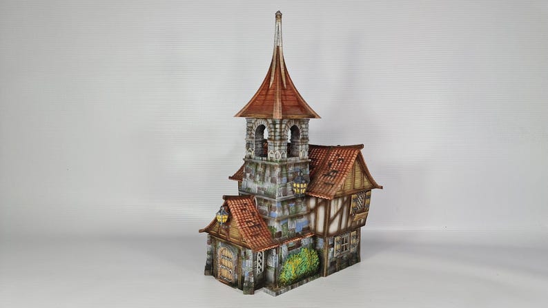 May include: A detailed miniature model of a medieval-style building. The structure features a tall central tower with a pointed roof, a stone facade, and a red tile roof. The building has multiple levels, windows, and decorative elements.