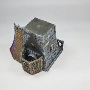 以下が含まれることがあります： 石造りのファサード、濃い灰色の屋根、木製のバルコニーを備えたミニチュアファンタジービル。 アーチ型の窓と紫色のアクセントがあります。 全体的なデザインは、中世またはゴシック様式を連想させます。