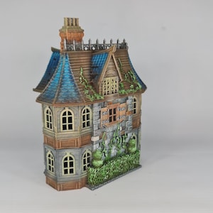 Op de afbeelding: Een gedetailleerd miniatuurhuis met een verweerde uitstraling. Het heeft een blauw en bruin dak, stenen muren en gewelfde ramen. Groen gebladerte accentueert de buitenkant en cre&euml;ert een gotische esthetiek. De schoorsteen is oranje.