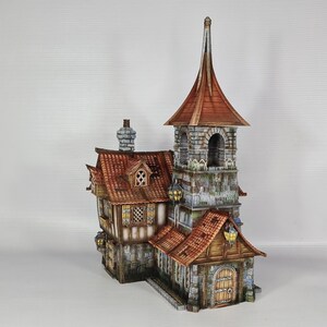May include: A detailed miniature model of a medieval-style building. The structure features a tall tower with a pointed roof, a stone facade, and a red tile roof. The building has multiple windows, a wooden door, and decorative lanterns.