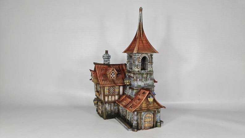 May include: A detailed miniature model of a medieval-style building. The structure features a tall tower with a pointed roof, a stone facade, and a red tile roof. The building has multiple windows, a wooden door, and decorative lanterns.