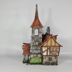 May include: A detailed miniature model of a medieval-style building with a tall steeple and a red tile roof. The building features stone and wood construction, with small windows and decorative details. The model includes a small garden.