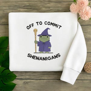 K&ouml;nnte beinhalten: Eine wei&szlig;e Keramik-Tasse mit schwarzem Henkel und dem Text "But First, Coffee" in fetter, schwarzer Schrift. Die Tasse ist mit einer dunklen Fl&uuml;ssigkeit gef&uuml;llt, wahrscheinlich Kaffee, und steht auf einer hellen Oberfl&auml;che.