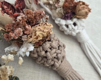 May include: Two macrame wall hangings featuring knotted cord in beige and white, each topped with a wooden ring. The knotted sections hold arrangements of dried flowers in shades of burgundy, rust, tan, and cream, finished with long tassels.