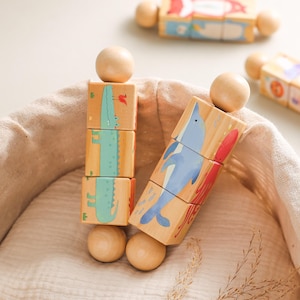 May include: Wooden animal blocks featuring a crocodile, dolphin, and other sea creatures. The blocks are painted in bright colors and have rounded wooden end pieces. The blocks are arranged on a beige cloth.