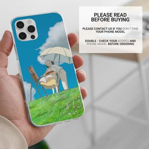 May include: Clear phone case featuring a vibrant anime scene of two figures under an umbrella on a grassy hill, with a blue sky and clouds. The case has a protective design and includes the text "PLEASE READ BEFORE BUYING".
