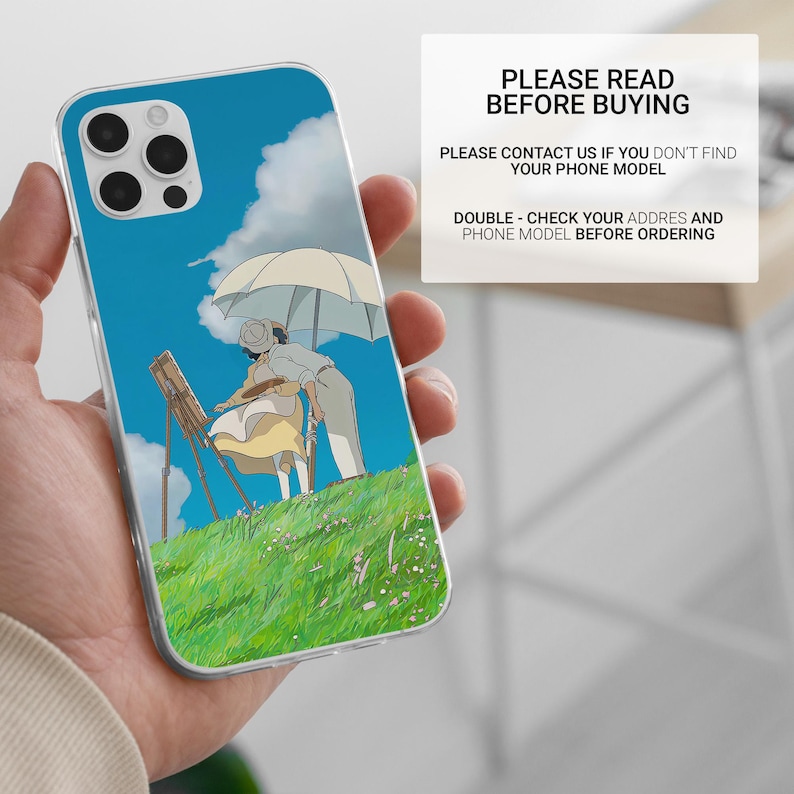 May include: Clear phone case featuring a vibrant anime scene of two figures under an umbrella on a grassy hill, with a blue sky and clouds. The case has a protective design and includes the text "PLEASE READ BEFORE BUYING".