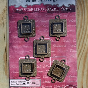 May include: A package of five square, bronze-colored bezels with decorative inner patterns. The package includes the text "Spellbinders media iXáge" and "SUSAN LENART KAZMER". The bezels are designed for crafting and mixed media projects.