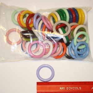 May include: A plastic bag filled with colorful plastic rings. The rings are in various colors, including red, yellow, green, blue, and white. There is one ring outside of the bag, which is a light purple color.