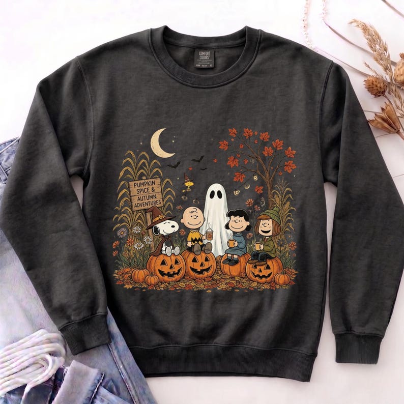 K&ouml;nnte beinhalten: Ein anthrazitfarbenes Sweatshirt mit Rundhalsausschnitt und einer Grafik von Peanuts-Figuren, die auf K&uuml;rbissen sitzen. Das Design zeigt eine Mondsichel, ein Schild mit der Aufschrift PUMPKIN SPICE & AUTUMN ADVENTURES, ein Gespenst und Herbstlaub.