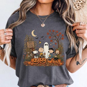 K&ouml;nnte beinhalten: Ein anthrazitfarbenes T-Shirt mit einem Grafikdruck von Snoopy, Charlie Brown und Freunden, die in einer herbstlichen Szene auf K&uuml;rbissen sitzen. Das Design zeigt ein Holzschild mit der Aufschrift PUMPKIN SPICE & AUTUMN ADVENTURES sowie einen Geist.
