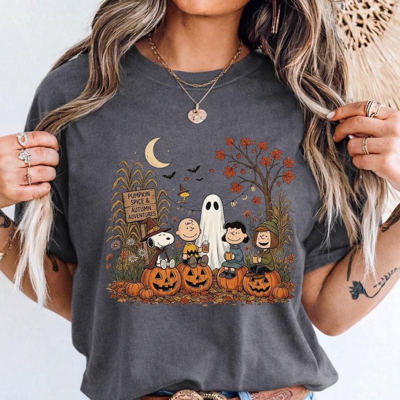 K&ouml;nnte beinhalten: Ein anthrazitfarbenes T-Shirt mit einem Grafikdruck von Snoopy, Charlie Brown und Freunden, die in einer herbstlichen Szene auf K&uuml;rbissen sitzen. Das Design zeigt ein Holzschild mit der Aufschrift PUMPKIN SPICE & AUTUMN ADVENTURES sowie einen Geist.