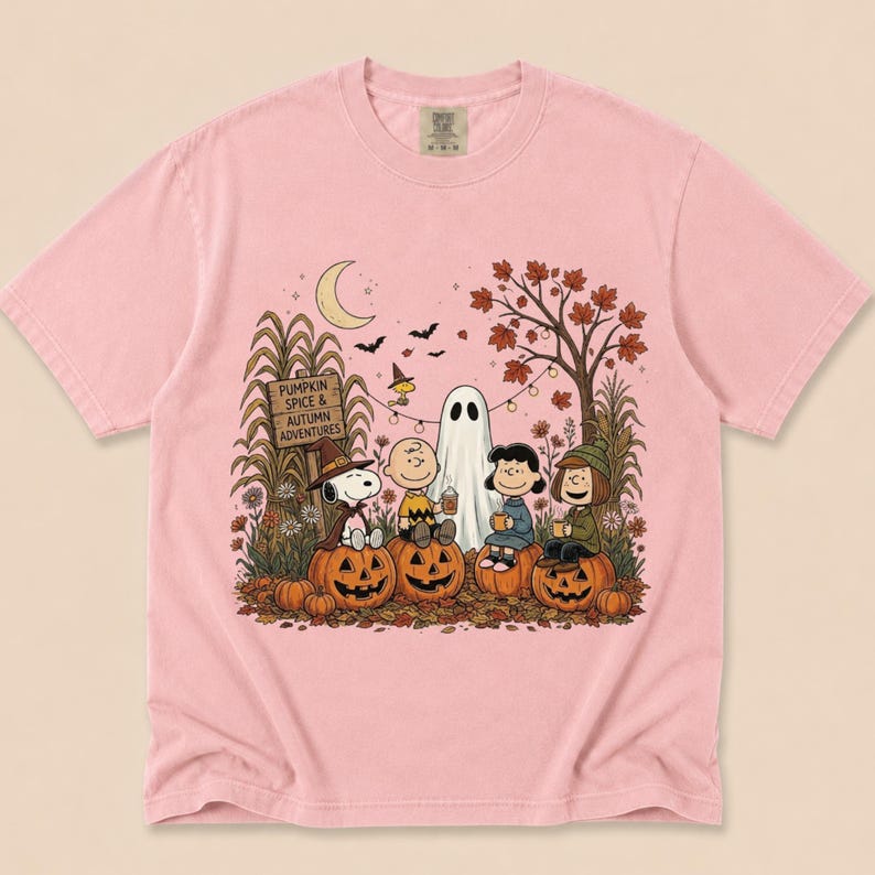 K&ouml;nnte beinhalten: Ein hellrosa T-Shirt mit einer Grafik von Peanuts-Figuren, die in einer herbstlichen Umgebung auf K&uuml;rbissen sitzen. Das Design zeigt ein Schild mit der Aufschrift PUMPKIN SPICE & AUTUMN ADVENTURES, einen Geist, eine Mondsichel und Laub.
