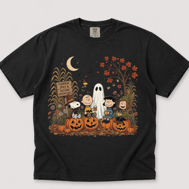 K&ouml;nnte beinhalten: Ein schwarzes Kurzarm-T-Shirt mit einer Grafik der Peanuts-Figuren in einem K&uuml;rbisfeld. Das Design zeigt Snoopy, Charlie Brown, Lucy und Linus mit einem Geist, K&uuml;rbissen und einem Schild mit der Aufschrift PUMPKIN SPICE & AUTUMN ADVENTURES.