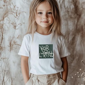May include: A young person wearing a white t-shirt with the text "YOR SOUL KIND" in a dark green square. The person is also wearing tan pants. The background is a neutral color.