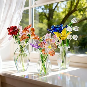 May include: Three glass vases with colorful glass flowers sit on a windowsill. The flowers include red roses, orange lilies, purple and orange blossoms, and blue and yellow tulips. The vases are clear with a ruffled top.