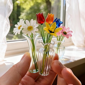 May include: A collection of miniature glass flower bouquets in clear vases. The flowers include daisies, tulips, and other colorful blooms in red, orange, yellow, blue, and pink. The vases have a ruffled rim.