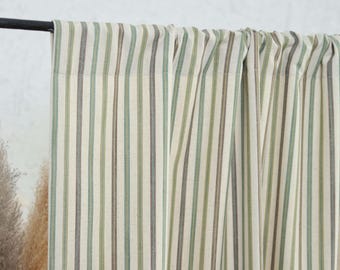 May include: Cream-colored curtains with vertical stripes in shades of green and brown. The curtains are hanging from a black rod, and the fabric has a textured appearance. The design is simple and suitable for a variety of interior styles.