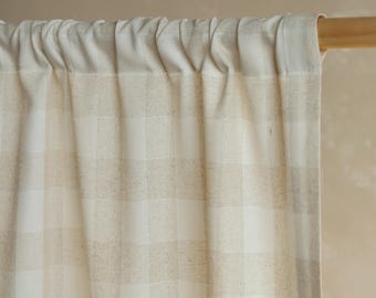May include: Cream-colored curtain with a checkered pattern. The fabric is a blend of white and tan squares, creating a neutral and textured look. The curtain is hanging from a wooden rod, with gathered fabric at the top.