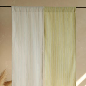 Puede incluir: Dos cortinas a rayas, una en crema con finas rayas azules y naranjas, la otra en amarillo pálido con finas rayas amarillas y verdes. Las cortinas cuelgan de una barra negra.