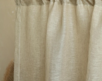May include: Beige linen curtain panel hanging from a wooden rod. The curtain has a textured appearance and is slightly translucent, allowing some light to pass through. The neutral color and simple design suggest a minimalist or natural aesthetic.