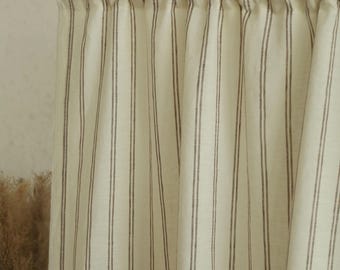 May include: Cream-colored curtain with vertical dark brown stripes. The fabric is gathered at the top and hangs in soft folds. The curtain is mounted on a wooden rod, suggesting a window treatment or room divider.