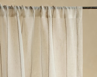 May include: Sheer, off-white linen curtains with vertical, dark gray stitched stripes. The curtains are hanging from a dark metal rod, creating a soft, natural light filter. The fabric has a slightly textured appearance.