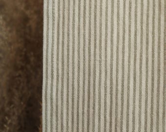 May include: Close-up of a fabric with vertical stripes. The stripes are a muted green color on a cream background. The fabric has a textured appearance, suggesting it may be linen or a similar material. The overall aesthetic is simple and classic.
