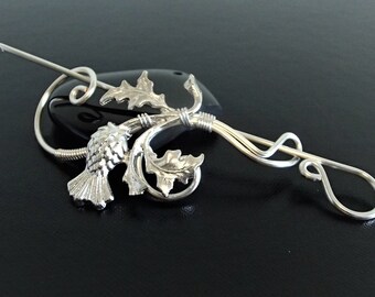 May include: Silver thistle brooch with a curled wire stem and a loop at the end. The thistle is detailed with a textured surface and a curled leaf.