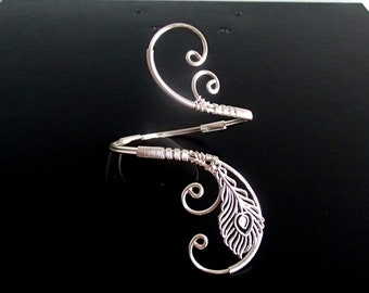 May include: Silver wire bracelet featuring a peacock feather design. The bracelet is open and adjustable.