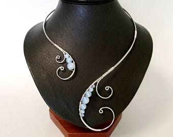 May include: A silver wire choker necklace with a delicate, curved design. The necklace is adorned with a row of light blue opal beads.