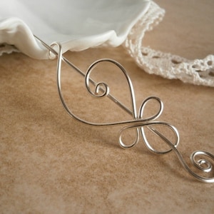 May include: Silver hair stick with a delicate, swirling design. The stick is made of thin wire and has a simple, elegant look.