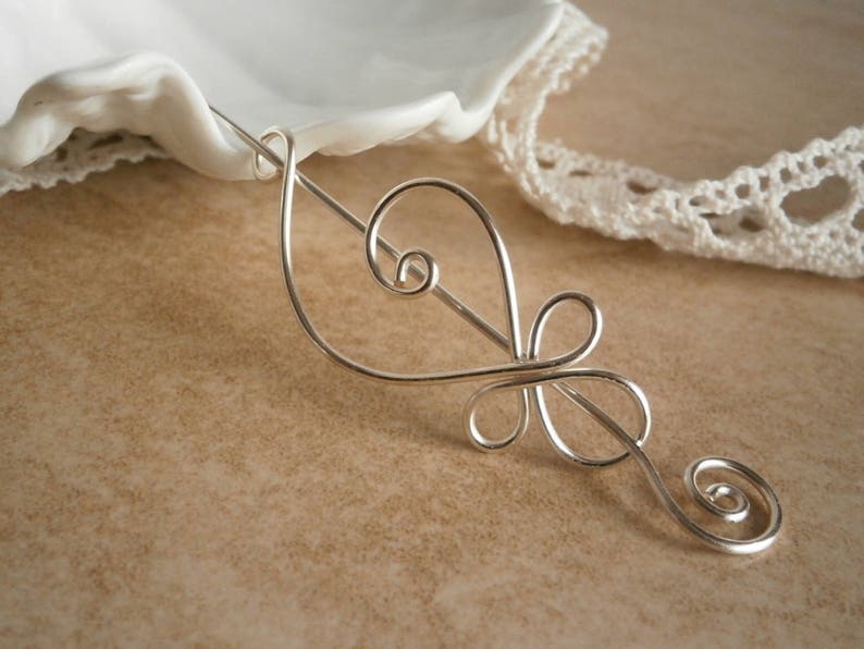 May include: Silver hair stick with a delicate, swirling design. The stick is made of thin wire and has a simple, elegant look.
