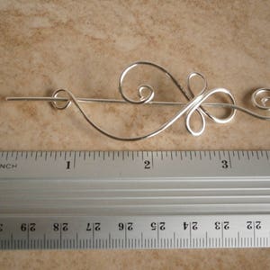 May include: Silver hair stick with a decorative swirl design, measuring approximately 3 inches in length.