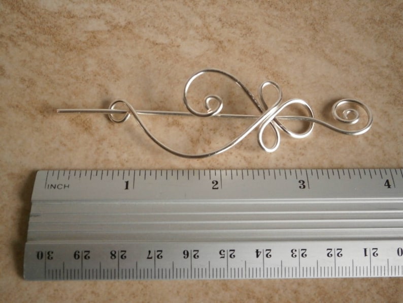 May include: Silver hair stick with a decorative swirl design, measuring approximately 3 inches in length.