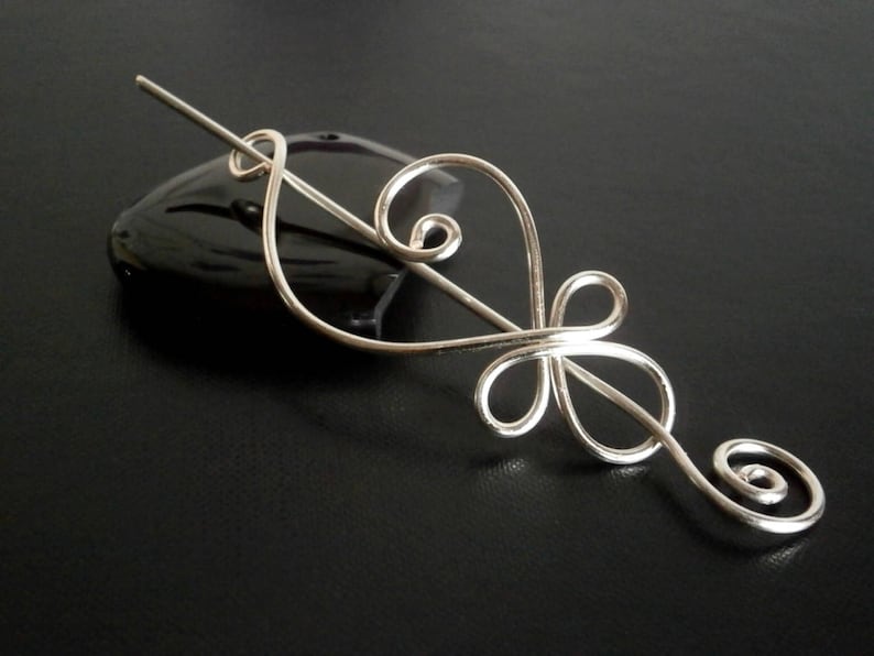 May include: Silver hair stick with a delicate, swirling design. The stick is thin and has a simple, elegant look.