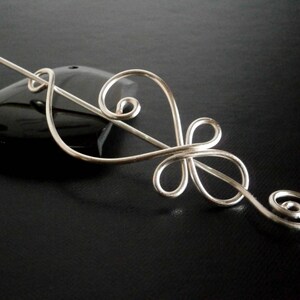 May include: Silver hair stick with a decorative design resembling a stylized flower. The stick is curved and has a smooth, polished finish.
