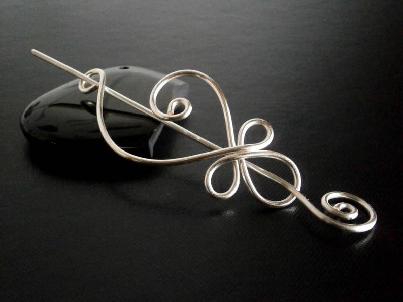 May include: Silver hair stick with a decorative design resembling a stylized flower. The stick is curved and has a smooth, polished finish.