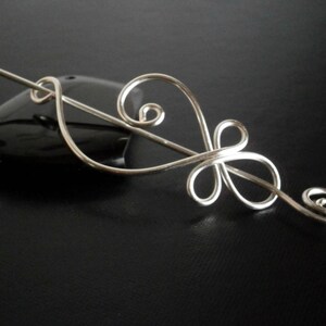 May include: Silver hair stick with a delicate, swirling design. The stick is made of thin wire and has a simple, elegant look.