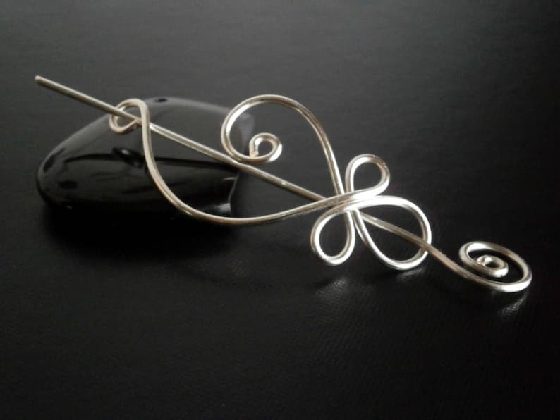 May include: Silver hair stick with a delicate, swirling design. The stick is made of thin wire and has a simple, elegant look.