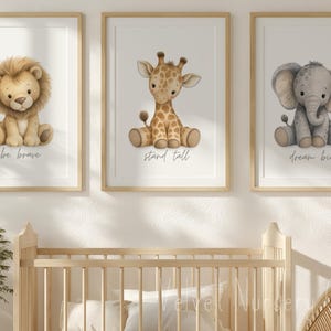 May include: Three framed watercolor prints featuring adorable safari animals. A lion with "be brave", a giraffe with "stand tall", and an elephant with "dream big". The prints have a soft, neutral color palette and are displayed above a wooden crib.