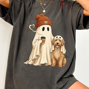 Peut inclure: Un t-shirt gris anthracite avec une impression graphique représentant un fantôme portant un bonnet marron et tenant une tasse de café, à côté d'un chien doré portant un drap de fantôme blanc sur la tête. Le motif est centré sur la poitrine.