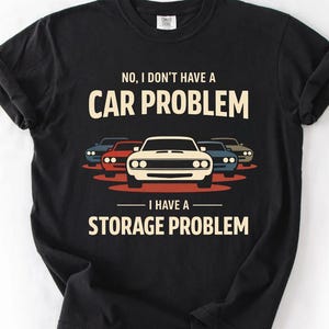 May include: Black t-shirt with the text "NO, I DON'T HAVE A CAR PROBLEM I HAVE A STORAGE PROBLEM." The graphic features a white car in the center with four other cars in the background.