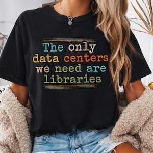 May include: A black short-sleeve t-shirt featuring the text "The only data centers we need are libraries" in multi-colored retro-style lettering. The graphic includes horizontal lines above and below the text in shades of orange, teal, and yellow.