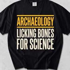 Peut inclure: Un t-shirt noir à manches courtes avec le texte jaune ARCHAEOLOGY centré au-dessus du texte blanc LICKING BONES FOR SCIENCE. Le motif est encadré par deux lignes horizontales jaunes, et le t-shirt possède un col rond standard.