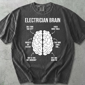 Peut inclure: T-shirt gris foncé avec l'inscription "ELECTRICIAN BRAIN" et un schéma de cerveau illustrant les pensées d'un électricien. Style décontracté et confortable.