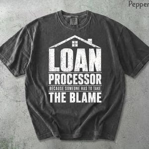 May include: Pepper-colored t-shirt with the text "LOAN PROCESSOR" in white, above the phrase "BECAUSE SOMEONE HAS TO TAKE THE BLAME." The design includes a house graphic. The shirt has short sleeves and a crew neck.
